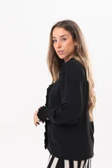 Camisa de manga larga color negro, con cuello camisero, cierre frontal con botones y detalle de volados en la cartera y los puños.