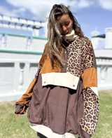 Buzo de estilo canguro con diseño de bloques de color y estampado animal print. Presenta una combinación de texturas en tonos marrón, chocolate y beige, con cuello alto, cierre frontal parcial con botones a presión y un bolsillo frontal grande con solapa.