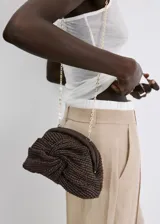 Bolso tipo clutch color marrón de tejido de fibra natural con diseño trenzado y nudo frontal. Cuenta con cierre de marco a presión y forro interior.