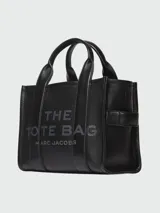 Bolso tote pequeño de cuero texturizado color gris con doble asa corta superior y correa larga extraíble y ajustable para llevar al hombro. Estampado frontal con el texto "The Tote Bag" y el nombre de la marca.