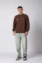 Buzo de cuello redondo en color arena, con diseño de calce regular y estampado gráfico minimalista en el pecho. Presenta puños y ruedo acanalados, con un pequeño detalle de etiqueta en el puño izquierdo.