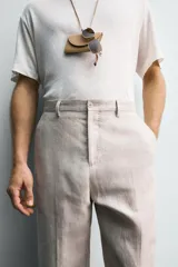 Pantalón de traje regular fit confeccionado en tejido de lino, con bolsillos laterales y bolsillos traseros de vivo con botón. Presenta cierre frontal con cremallera y botón.