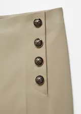 Pantalon de corte skinny en color beige, confeccionado en mezcla de algodón. Presenta un diseño crop con botones decorativos en la parte frontal, cierre oculto de cremallera y gancho, bolsillos laterales y bolsillos de ribete en la parte posterior.
