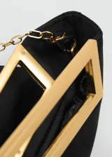 Bolso de mano tipo sobre con diseño cuadrado, confeccionado en poliéster negro. Cuenta con un asa metálica rígida en tono dorado y una cadena larga extraíble.