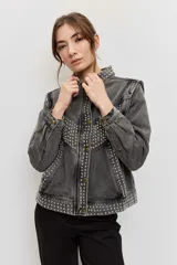 Campera de jean color gris con efecto acid wash, corte clásico y cierre frontal de botones metálicos. Presenta cuello camisero, bolsillos ribeteados y está decorada con apliques de tachas plateadas en el cuello, el canesú frontal, los bordes de la botonera, los bolsillos y el ruedo.