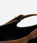 Zapatilla tipo Mary Jane color marrón con efecto gamuzado, tira fina con hebilla ajustable sobre el empeine y pequeñas tachuelas metálicas doradas. Tiene punta redonda y suela baja.