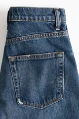 Jean tobillero de cinco bolsillos en denim de algodón rígido, con piernas de volumen curvo, corte estándar y tiro alto con cierre de botones.