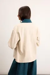 Sobrecamisa de algodón color beige, de corte holgado, con bolsillos frontales aplicados, cuello camisero y puños en contraste con estampado de cuadros en tonos verde oscuro. Cuenta con cierre frontal de botones metálicos.