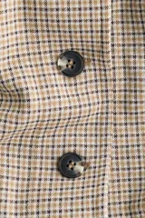 Chaleco largo sin mangas con cuello redondo y cierre frontal de botones. Presenta un diseño de tejido jacquard con patrón de cuadros pequeños y costuras verticales que definen la silueta.