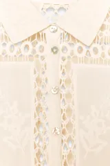 Blusa de algodón color crudo con detalle de bordados y crochet. Cuello redondo, manga corta y cierre frontal con botones.