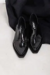 Mocasines de charol color bordó, de diseño vanguardista con corte asimétrico en el empeine, abertura en V, punta fina y suela plana con pequeño tacón.