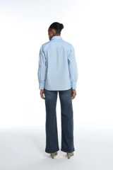 Camisa clásica celeste de tricolina con diseño de líneas limpias, cuello camisero, mangas largas y detalles bordados decorativos en el frente.