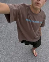Remera marrón oversize con diseño gráfico estampado en la espalda que incluye la inscripción "Kaboa" y fechas de gira mundial.