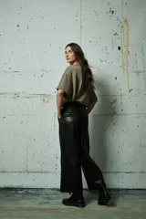 Pantalón de cuero sintético negro de corte ancho y tiro alto, con costuras verticales decorativas en el frente y cierre frontal con botón.