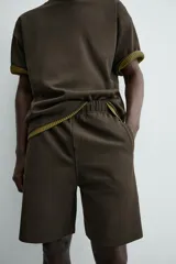 Bermuda de hombre color verde oscuro, de corte relajado y tiro medio. Confeccionada en tejido texturado, presenta cintura elástica con cordón de ajuste interno y bolsillos laterales y trasero de vivo.