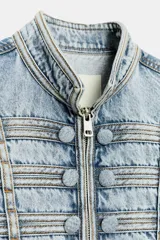 Chaqueta de denim con efecto lavado, corte entallado y cuello redondo. Presenta un diseño de estilo militar con cierre frontal de cremallera metálica y aplicaciones decorativas de botones y costuras en el delantero y los puños.