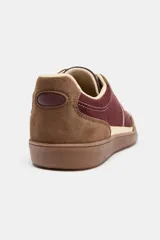 Zapatillas deportivas de caña baja con combinación de colores y materiales. El cuerpo principal es de color bordó, con refuerzos en gamuza marrón y detalles en color crema. La suela es de goma marrón. El cierre es mediante cordones gruesos color crema.