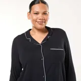 Conjunto de pijama de dos piezas compuesto por una camisa de manga larga con botones frontales y cuello solapa, y un pantalón de corte recto. Ambas prendas presentan un diseño liso en color negro con detalles de ribetes en contraste.