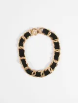 Collar tipo gargantilla de eslabones gruesos dorados entrelazados con una cinta de terciopelo negro.