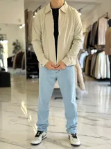 Campera de gabardina beige de corte boxy fit, con cuello camisero, cierre frontal de cremallera blanca y bolsillos laterales ribeteados.