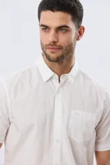 Camisa lisa de algodón azul marino, de manga corta, con cuello camisero, cierre frontal de botones y un bolsillo aplicado en el pecho.