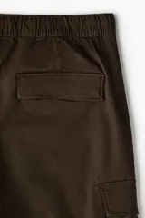 Pantalón cargo slim fit marrón, con cintura elástica ajustable mediante cordón, bolsillos laterales con solapa y costuras decorativas en las rodillas.