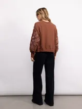 Buzo de algodón color negro con cuello redondo, mangas largas y bordado floral XL en color cobre en las mangas. Presenta un diseño holgado y cómodo.