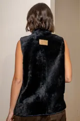 Chaleco de cuero azul con acabado gamuzado, cuello alto con forro de piel sintética negra, cierre frontal con botones tipo toggle y bolsillos laterales amplios.