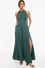 Vestido largo azul marino, de corte fluido, con escote halter, detalles trenzados en los hombros, bolsillos laterales y tajo profundo en la pierna.