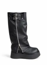 Bota bucanera de caña alta estilo polaina, confeccionada en cuero sintético negro, con plataforma gruesa, cierre lateral metálico y doble hebilla decorativa en la parte superior.