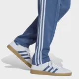 Pantalón deportivo Adidas de corte clásico, color azul con las icónicas tres tiras blancas laterales. Presenta el logo del Trifolio bordado en la parte superior y cordón de ajuste en la cintura.