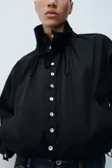 Cazadora de algodón negra con cuello subido ajustable con lazadas, manga larga, bolsillos de vivo en los laterales y bajo ajustable con cordones. Cierre frontal con botones.