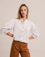 Blusa blanca con cuello mao, tajos laterales y botones frontales. Mangas largas abullonadas con puños elásticos.
