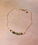 Collar de cadena fina dorada con una serie de cuentas centrales que combinan piedras naturales en tonos tierra, verde y gris con esferas metálicas doradas.