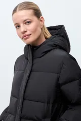 Campera puffer larga de color negro, con diseño capitoneado, capucha integrada y cierre frontal oculto. Presenta cierres laterales en el ruedo para mayor comodidad.