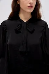 Camisa de poliéster color marfil, de diseño holgado, con cuello alto lazada y mangas largas abullonadas.