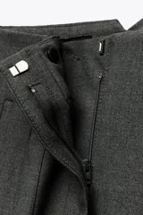 Pantalón tobillero gris oscuro de tiro alto con costuras marcadas en delantero y espalda, bolsillos delanteros de vivo y cierre frontal con cremallera, botón interior y gancho metálico.