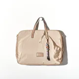 Bolso tipo tote color beige, con cierre superior y doble asa corta. Incluye un charm colgante con cuentas de colores y flecos.