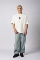 Remera oversize de algodón 100% premium, color blanco hueso, con bordado frontal "90's" en negro y un parche trasero con una imagen estilo videoclip de Nirvana.