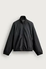 Cazadora relaxed fit confeccionada en denim de algodón color negro, con cuello subido y cierre frontal de cremallera. Cuenta con mangas largas, bolsillos laterales en las costuras y acabados con elástico en puños y cintura, con efecto lavado.