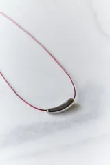 Gargantilla minimalista compuesta por un hilo encerado fino y un dije central de acero quirúrgico en forma de tubo curvo.