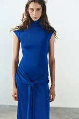 Vestido largo color azul, confeccionado en tejido elástico, con cuello alto, manga muy corta y detalle de lazada en la cintura. Cuenta con abertura en la espalda.