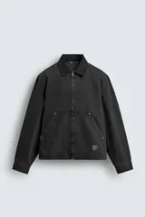 Cazadora de algodón color negro lavado, de corte relajado (relaxed fit), con cuello solapa a contraste, cierre frontal de cremallera, bolsillos canguro en la cadera y puños con botón a presión.