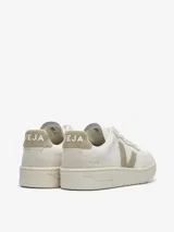 Championes Veja modelo V-90, de diseño urbano con silueta de perfil bajo. Confeccionados en cuero blanco con detalles en gamuza color beige en los laterales, talón y puntera. Presentan suela plana de goma y cierre con cordones.