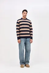 Buzo de punto con diseño de rayas horizontales en azul marino y beige, cuello redondo y puños acanalados. Presenta un pequeño bordado de estrella en la manga.