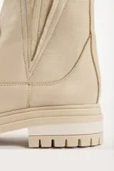 Bota tipo chelsea de caña media en color beige, con suela track dentada y paneles laterales elásticos acanalados.