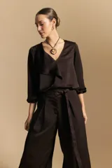 Blusa negra de satén con escote en V y detalle de volados frontales. Presenta mangas largas con puños abotonados y una silueta fluida.