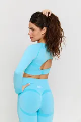 Conjunto deportivo de dos piezas color turquesa, compuesto por un top de manga larga con cuello redondo y detalle de textura en el pecho, y calzas de tiro alto. Ambas prendas presentan un diseño sin costuras con detalles texturizados y logo estampado en el top.