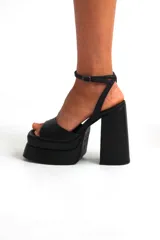 Sandalias negras de cuero sintético, con plataforma y taco cuadrado. Tira delantera ancha y pulsera al tobillo con hebilla.