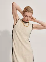 Vestido midi tejido color crema con ribete negro en cuello, sisas y ruedo. Presenta aberturas laterales en el ruedo.